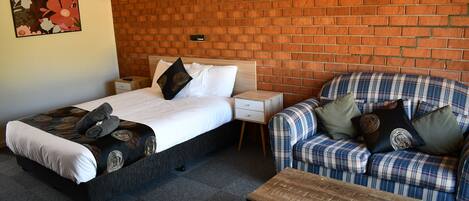 Una habitación con cama, sofá, una mesa de centro de madera y una pared de ladrillo.