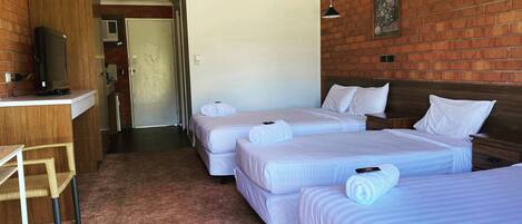 Habitación de hotel con dos camas, un escritorio, un televisor, un ventilador de techo y una pared de ladrillo.