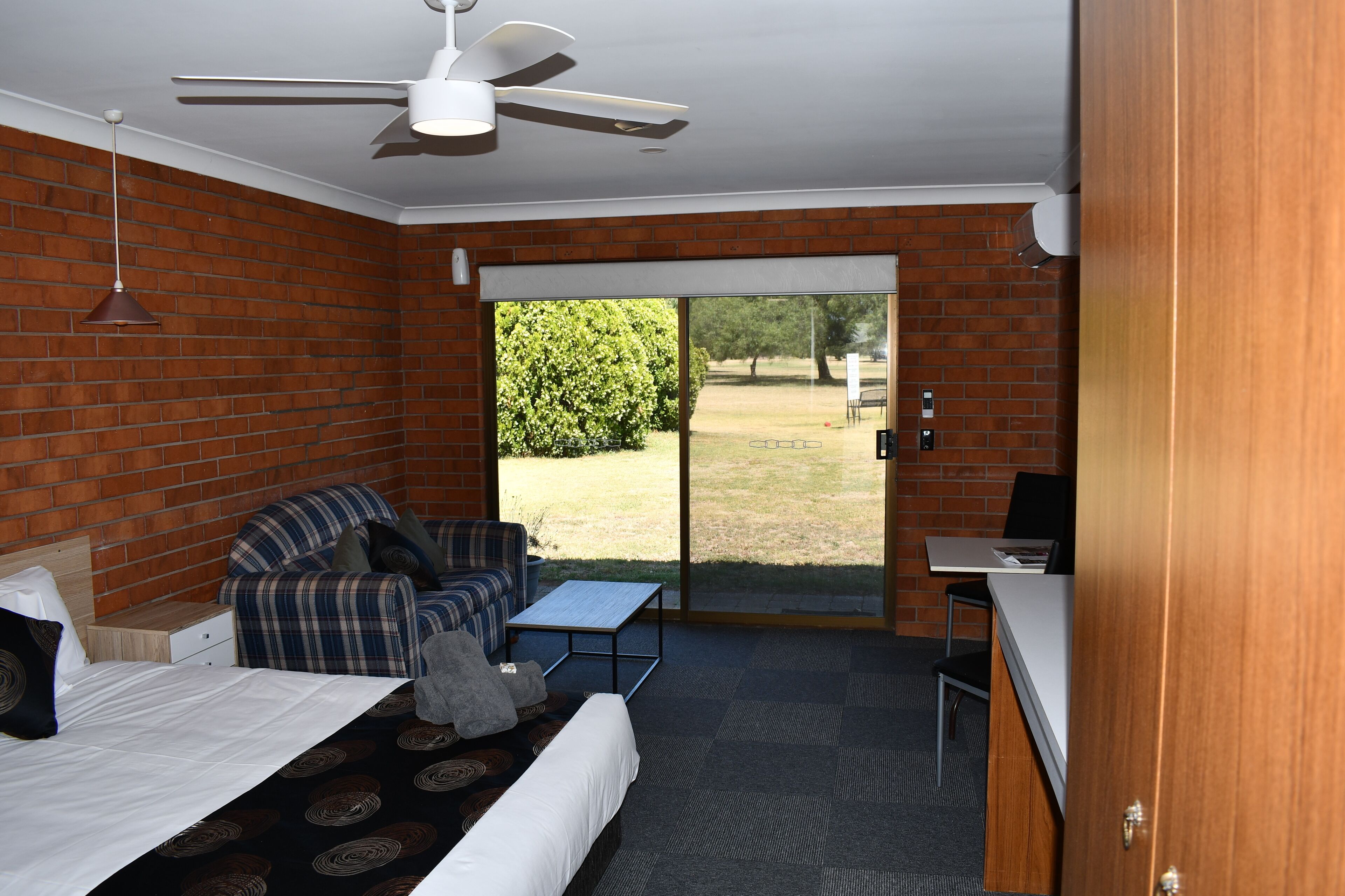 A room with a bed, a sofa, a small table, a desk, and a sliding glass door leading to an outdoor area.