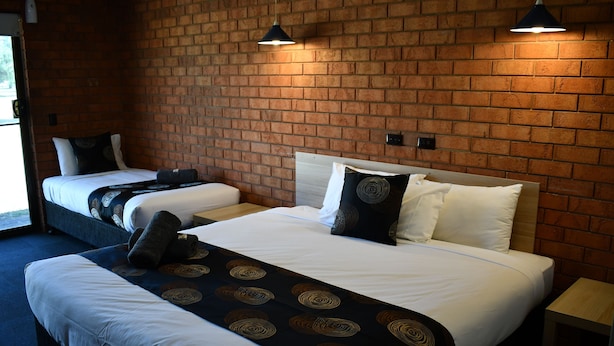 Une chambre d’hôtel avec deux lits, un mur en briques et une petite table de chevet en bois.