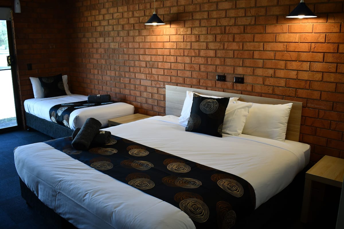 Une chambre d’hôtel avec deux lits, un mur en briques et une petite table de chevet en bois.