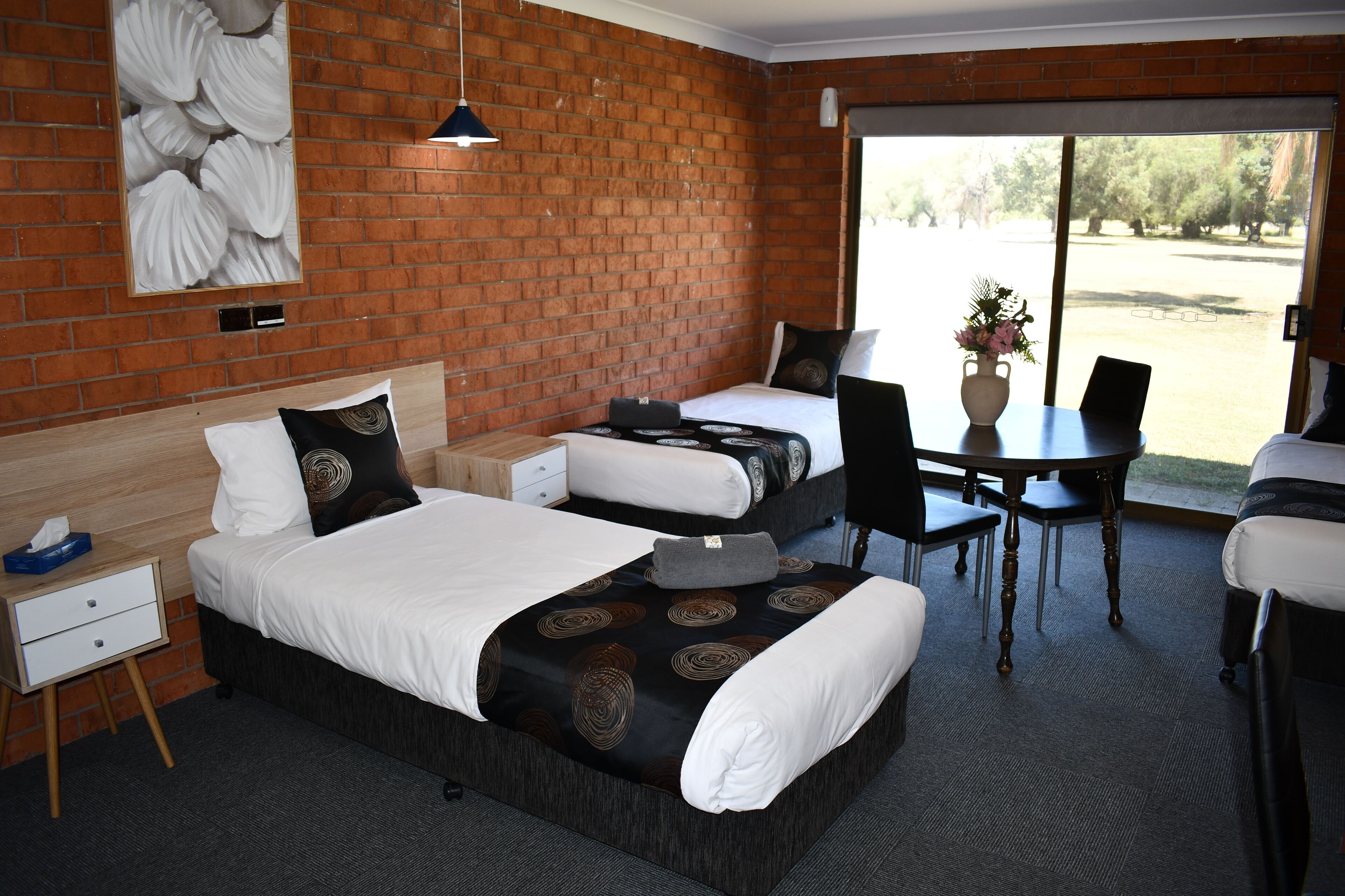A hotel room with two beds, a dining table, chairs, a small desk, and a large window with a view of the outdoors.