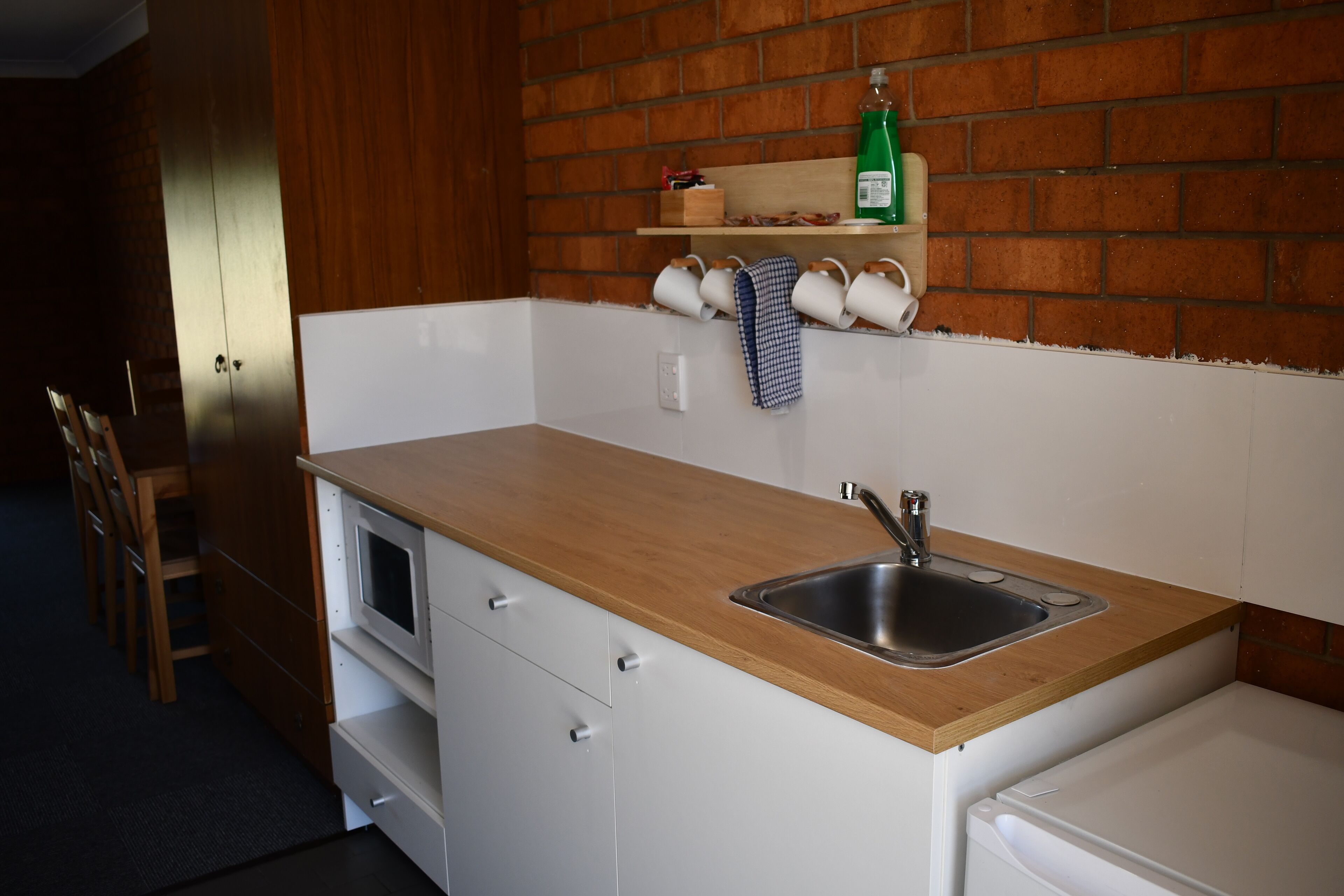 A compact kitchen with a wooden countertop, a built-in sink, and a brick backsplash.