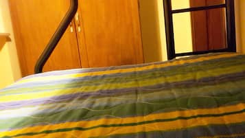 A bed with a striped blanket, a wooden wardrobe, and a mirror on the wall.