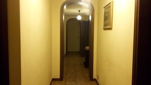 A narrow hallway with a door at the end, a light fixture above, and a framed picture on the wall. - Gessy's (Lucca)