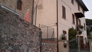A stone wall with a metal gate, a building with a pink facade and wooden shutters, and a number '167' sign. - Gessy's (Lucca)