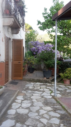 A stone-paved courtyard with a wooden door, potted plants, and purple flowering bushes. - Gessy's (Lucca)