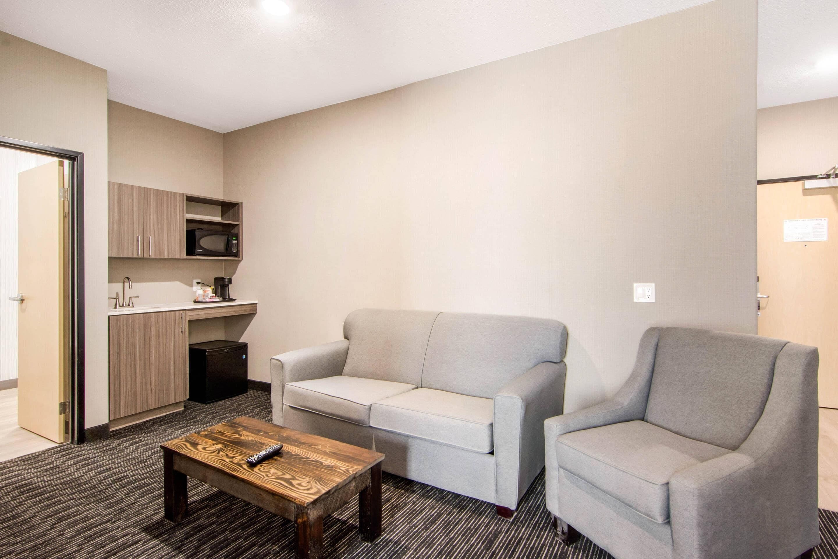 Un espacio habitable compacto con kitchenette, un sofá gris, un sillón a juego y una mesa de centro de madera.