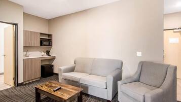 Un espacio habitable compacto con kitchenette, un sofá gris, un sillón a juego y una mesa de centro de madera.