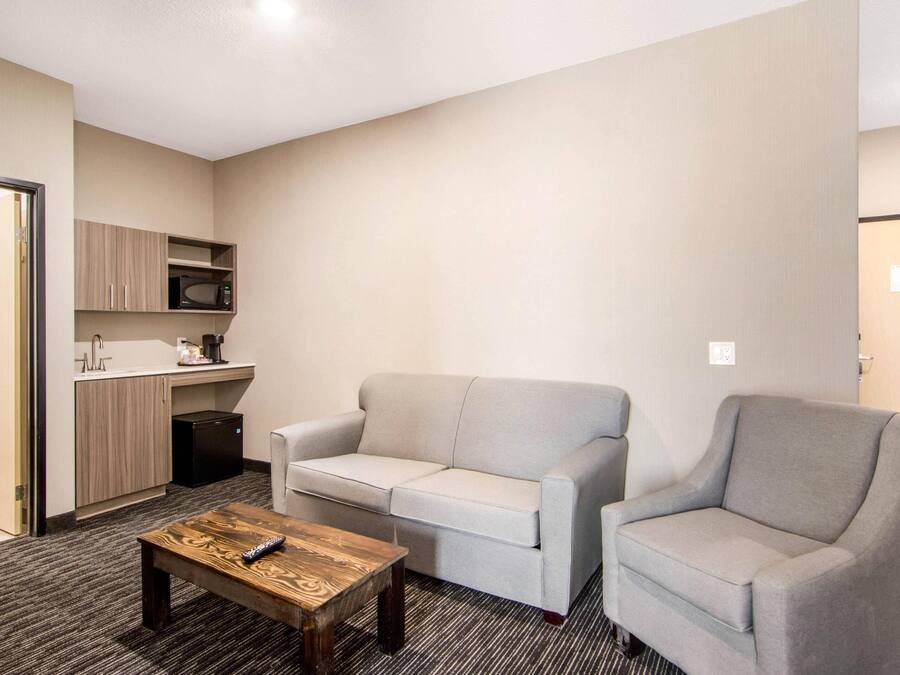Un espacio habitable compacto con kitchenette, un sofá gris, un sillón a juego y una mesa de centro de madera.