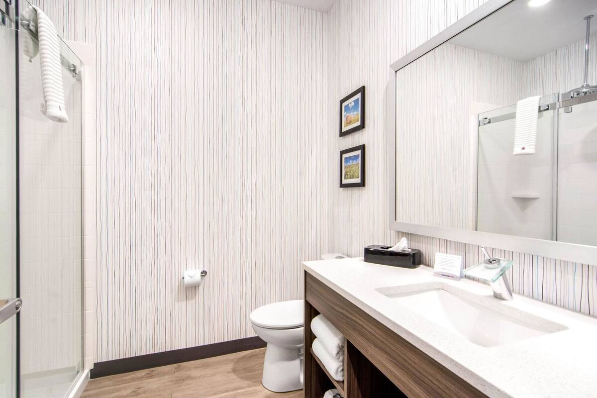 A modern bathroom with a striped wallpaper, a white toilet, a large mirror, and a glass shower enclosure.