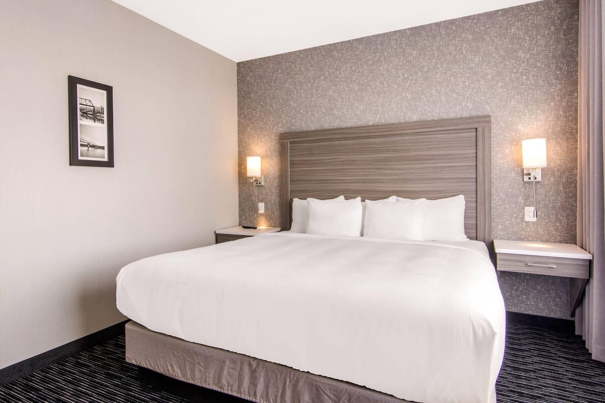 A hotel room with a large bed, two bedside tables, a headboard, and a framed picture on the wall.