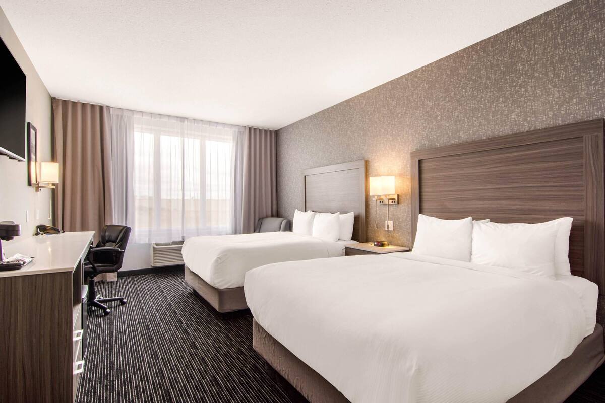 A hotel room with two beds, a desk, a chair, and a large window with curtains.