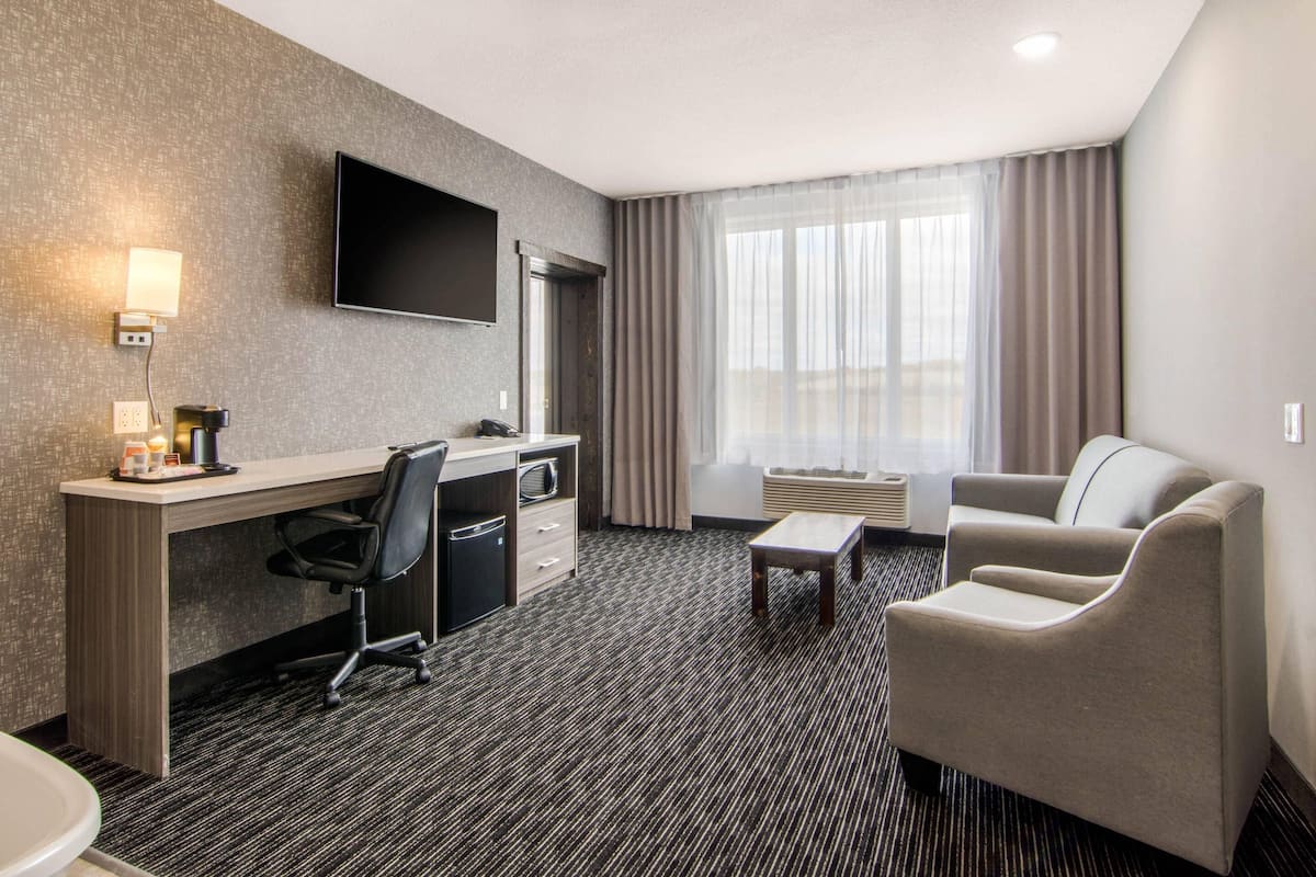 A hotel room with a desk, chair, sofa, TV, and large window with curtains.