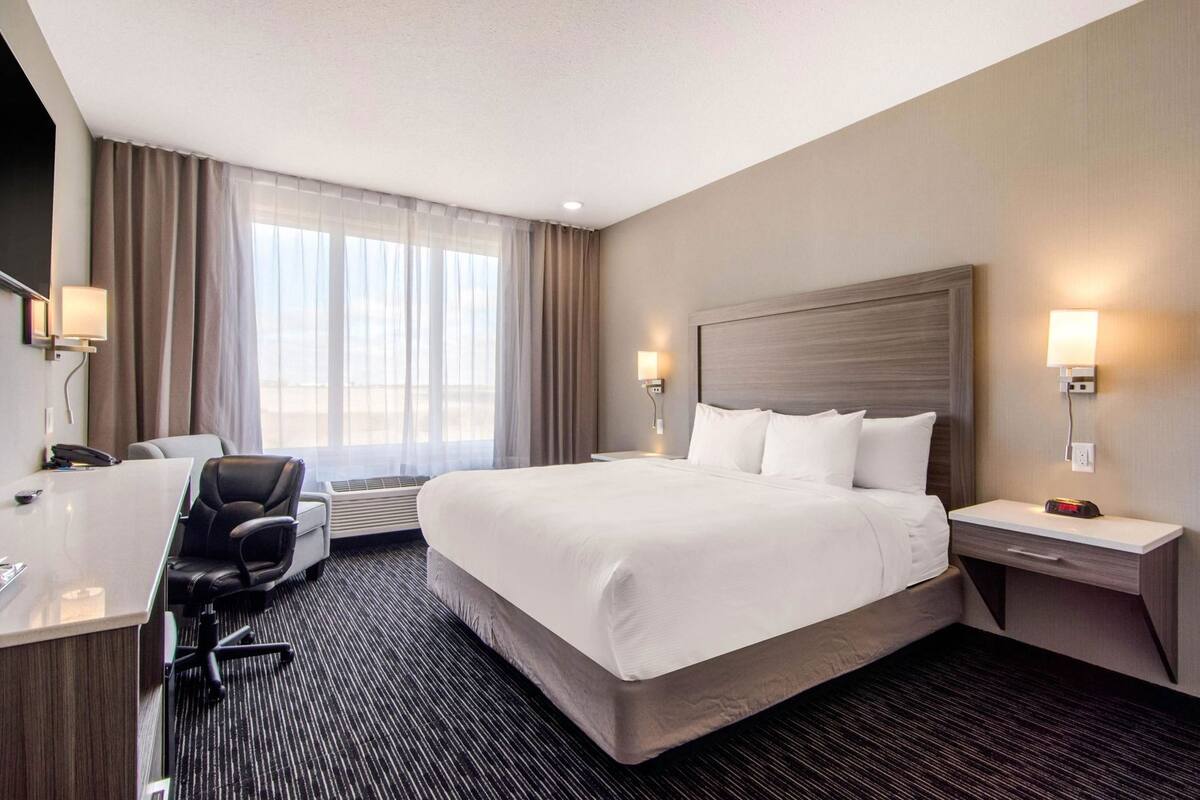 A hotel room with a large bed, a desk with a chair, a desk lamp, and a wall-mounted lamp.