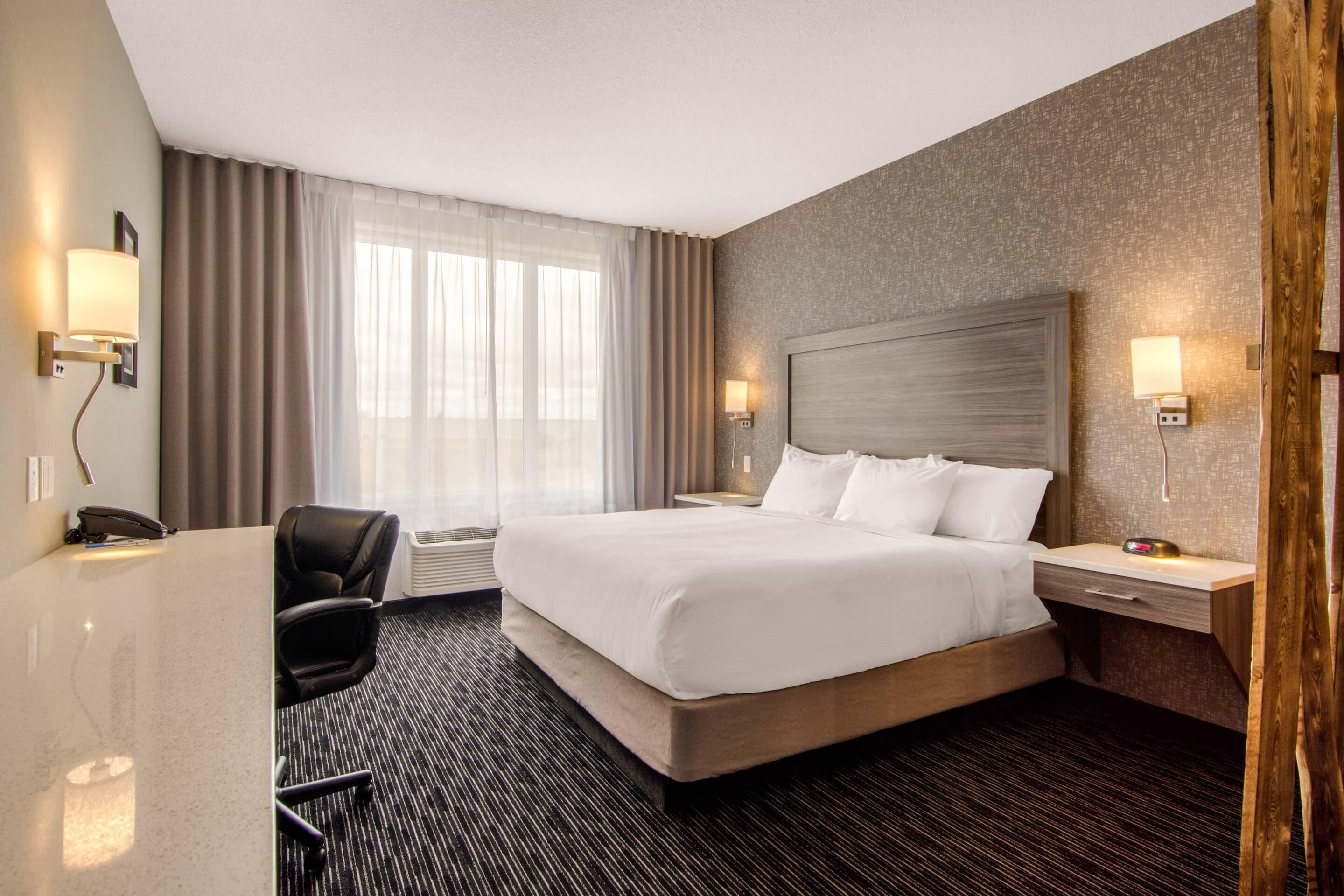 A hotel room with a large bed, a desk with a chair, a telephone, and two bedside lamps.