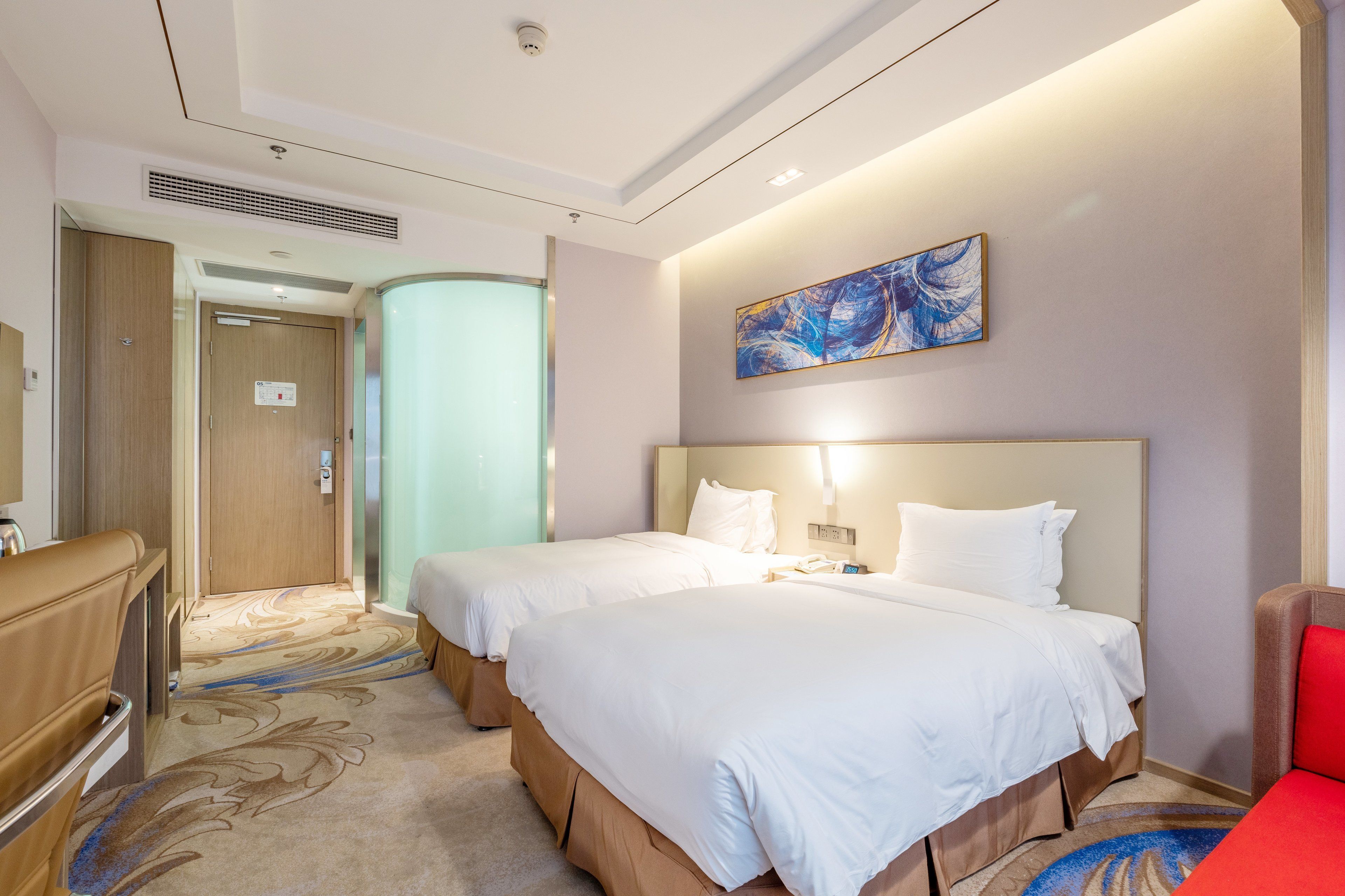 A hotel room with two beds, a red chair, a desk, and a painting on the wall.