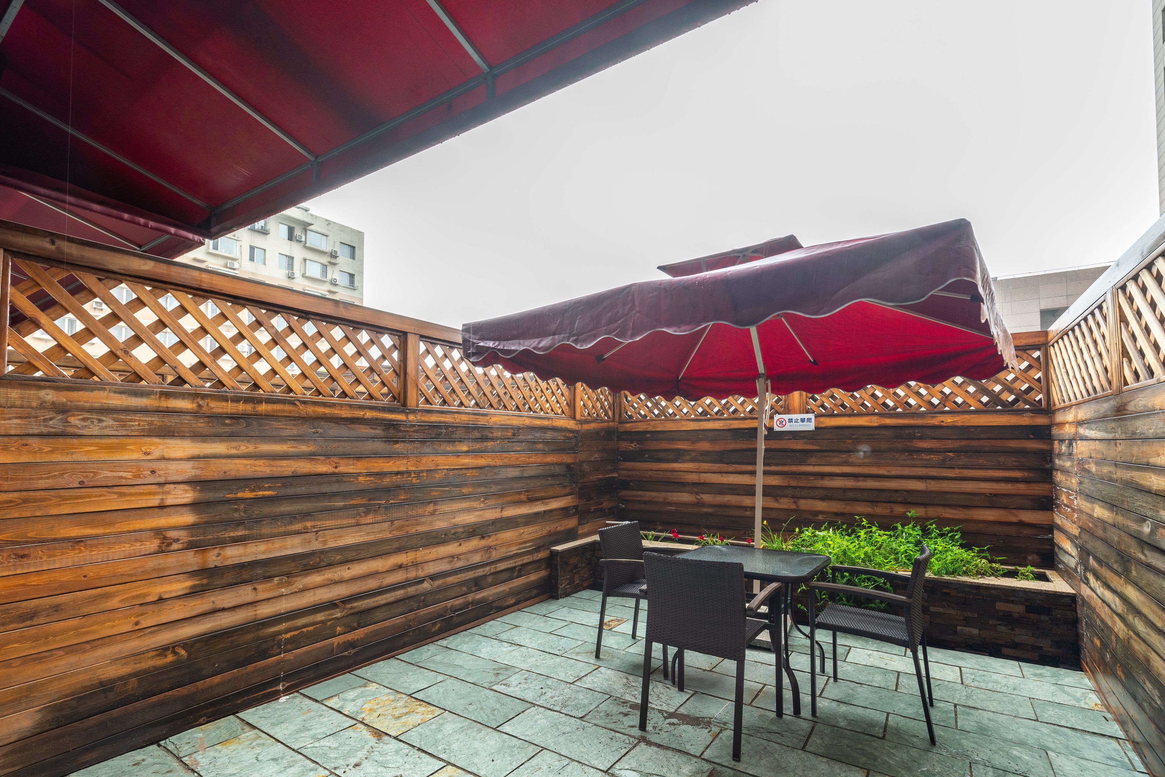 A wooden deck with a table and chairs, a red umbrella, and a wooden fence.