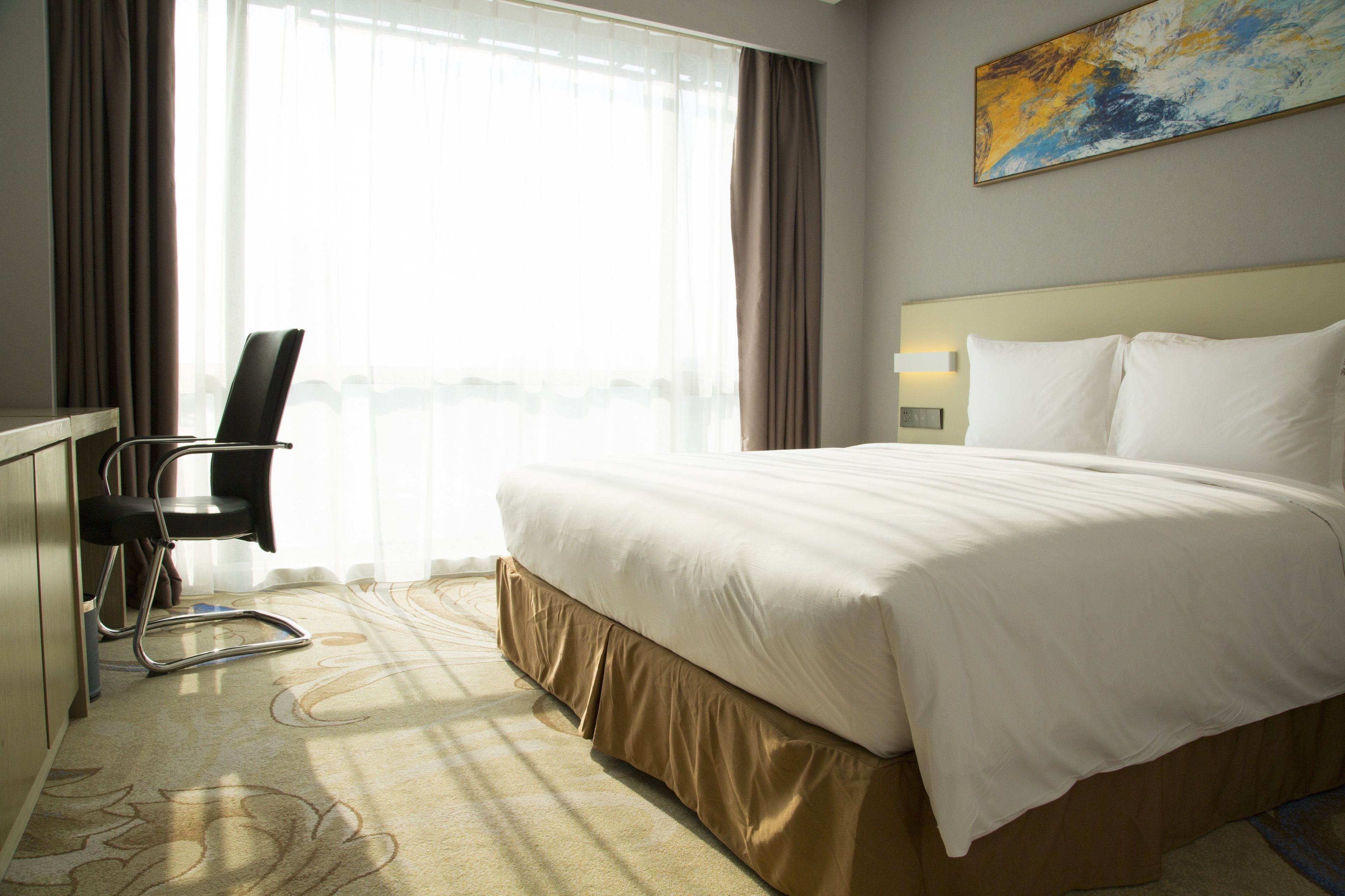 A hotel room with a bed, a desk, a chair, and a large window with curtains.