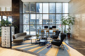 A modern lobby with a curved sofa, armchairs, a coffee table, and a small table with two monitors. Large windows offer a view of the cityscape. - Holiday Inn Express Anshan Downtown by IHG (Anshan)