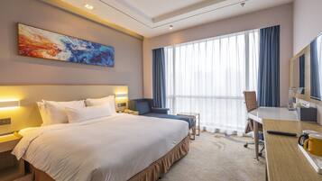 A hotel room with a large bed, a desk, a chair, a desk lamp, a television, and a window with curtains.