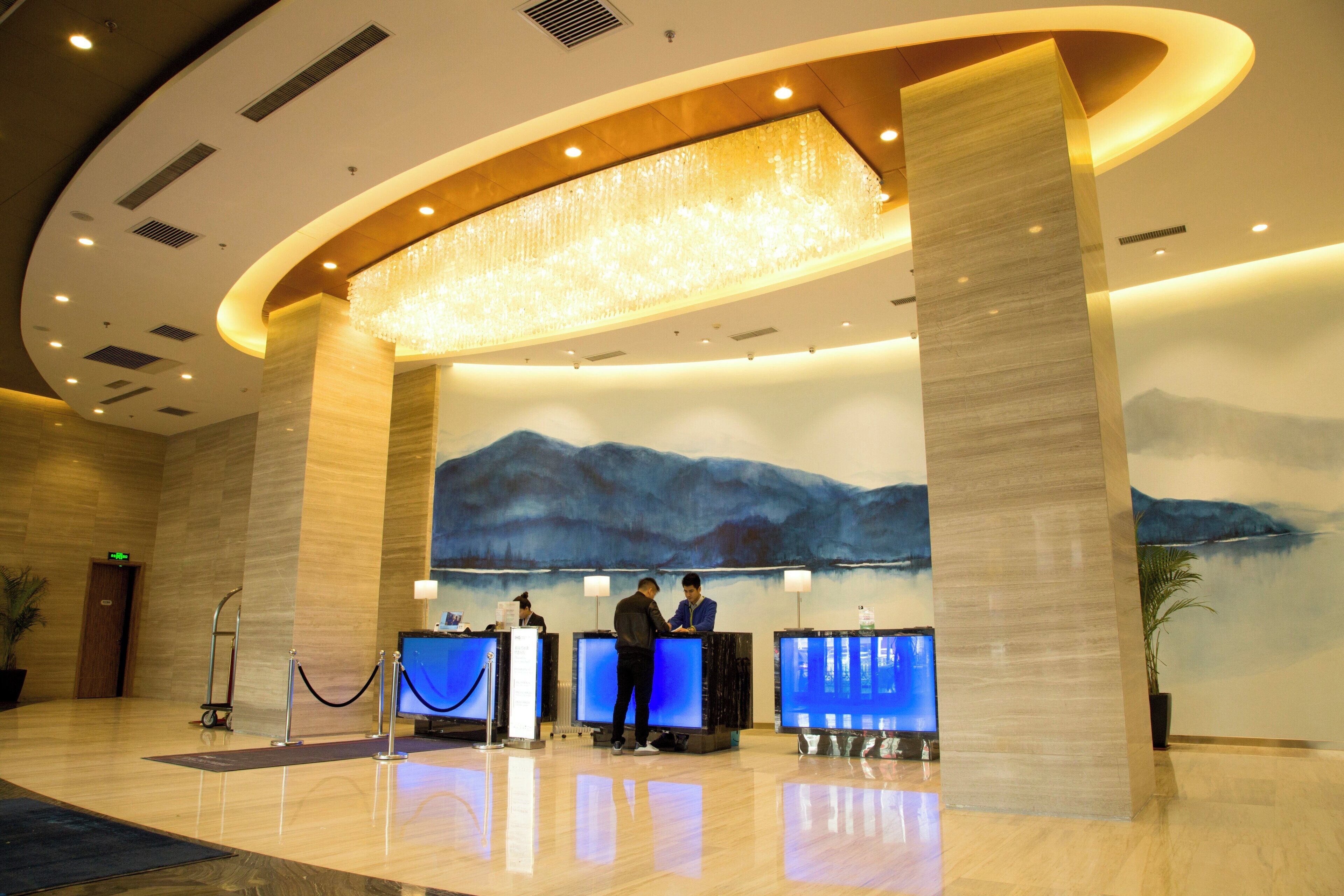 A hotel reception area with a large chandelier, a reception desk, and a wall mural.