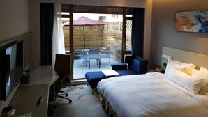 A hotel room with a bed, a desk, a chair, a small table, and a view of an outdoor patio area. - Holiday Inn Express Anshan Downtown by IHG (Anshan)