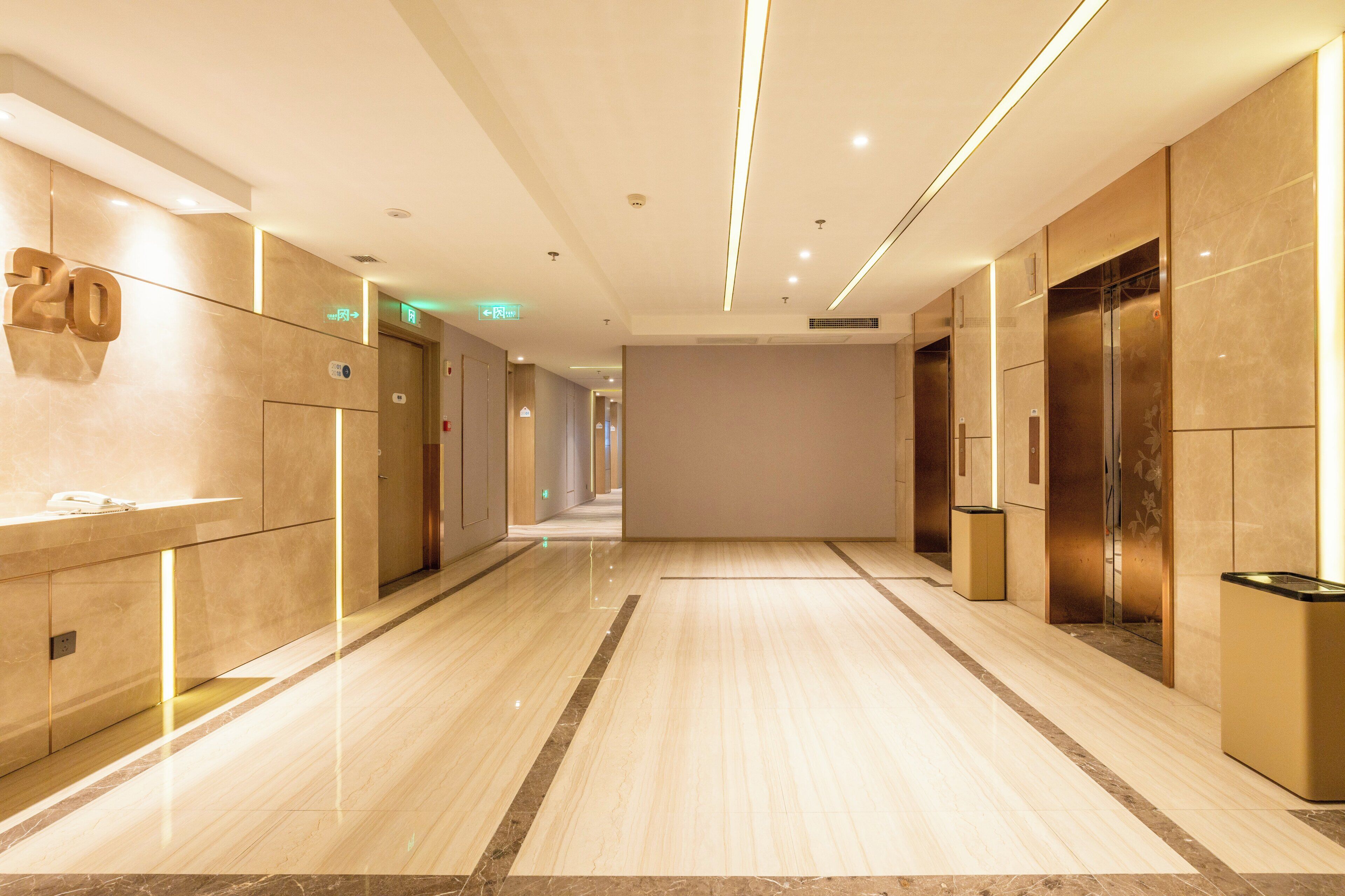 Pasillo de hotel con pisos de mármol, ascensores y una zona de recepción con un teléfono y un cartel que indica el año 2018.