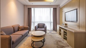 A modern hotel room with a sofa, armchair, round coffee table, and a flat-screen TV mounted on the wall. - Holiday Inn Express Anshan Downtown by IHG (Anshan)