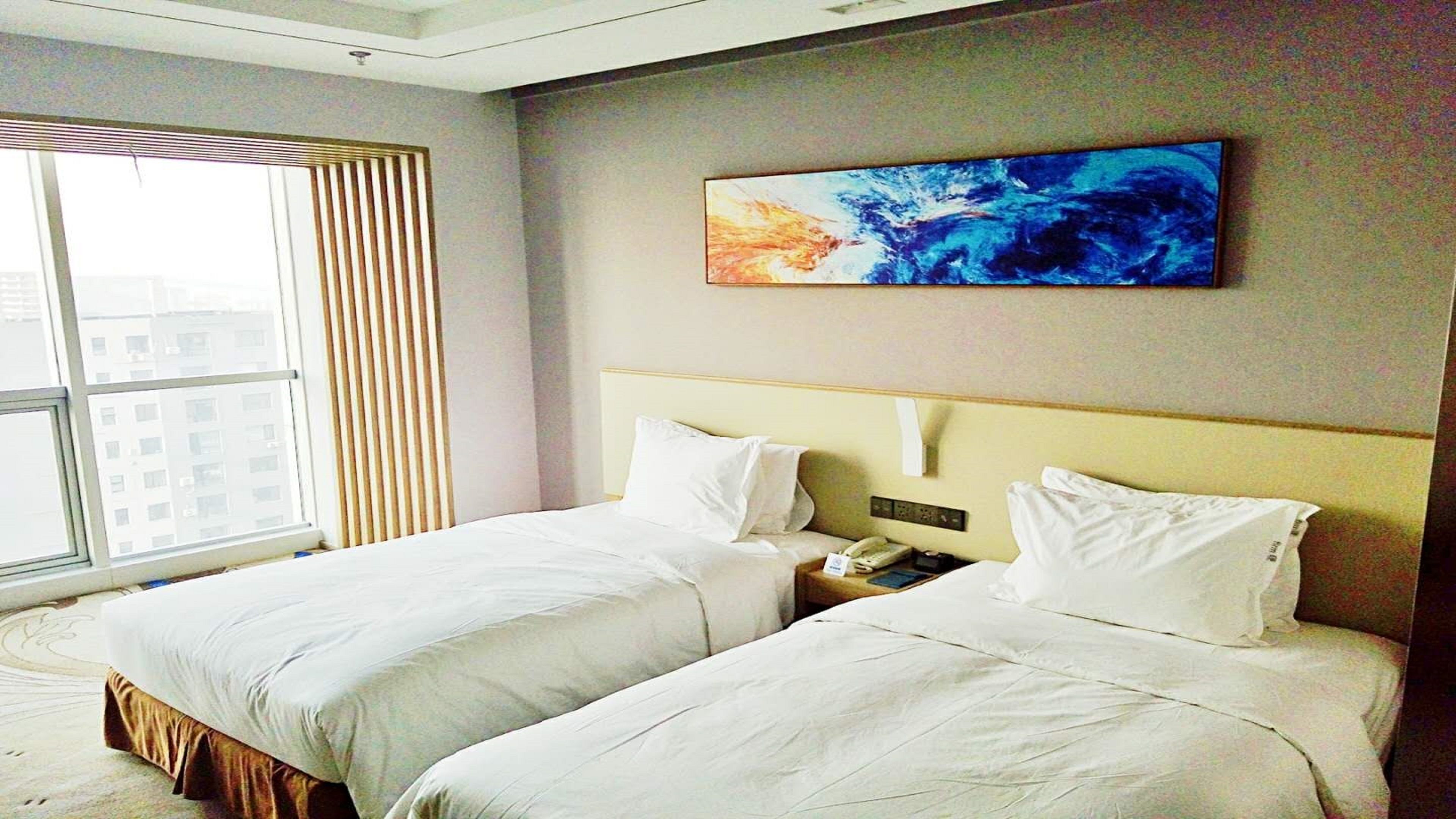 A hotel room with two beds, a large window, and a painting on the wall.