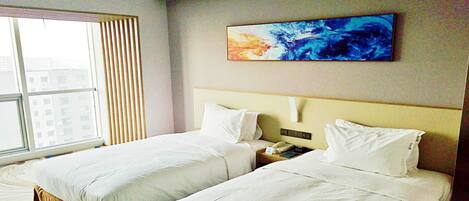 A hotel room with two beds, a large window, and a painting on the wall.