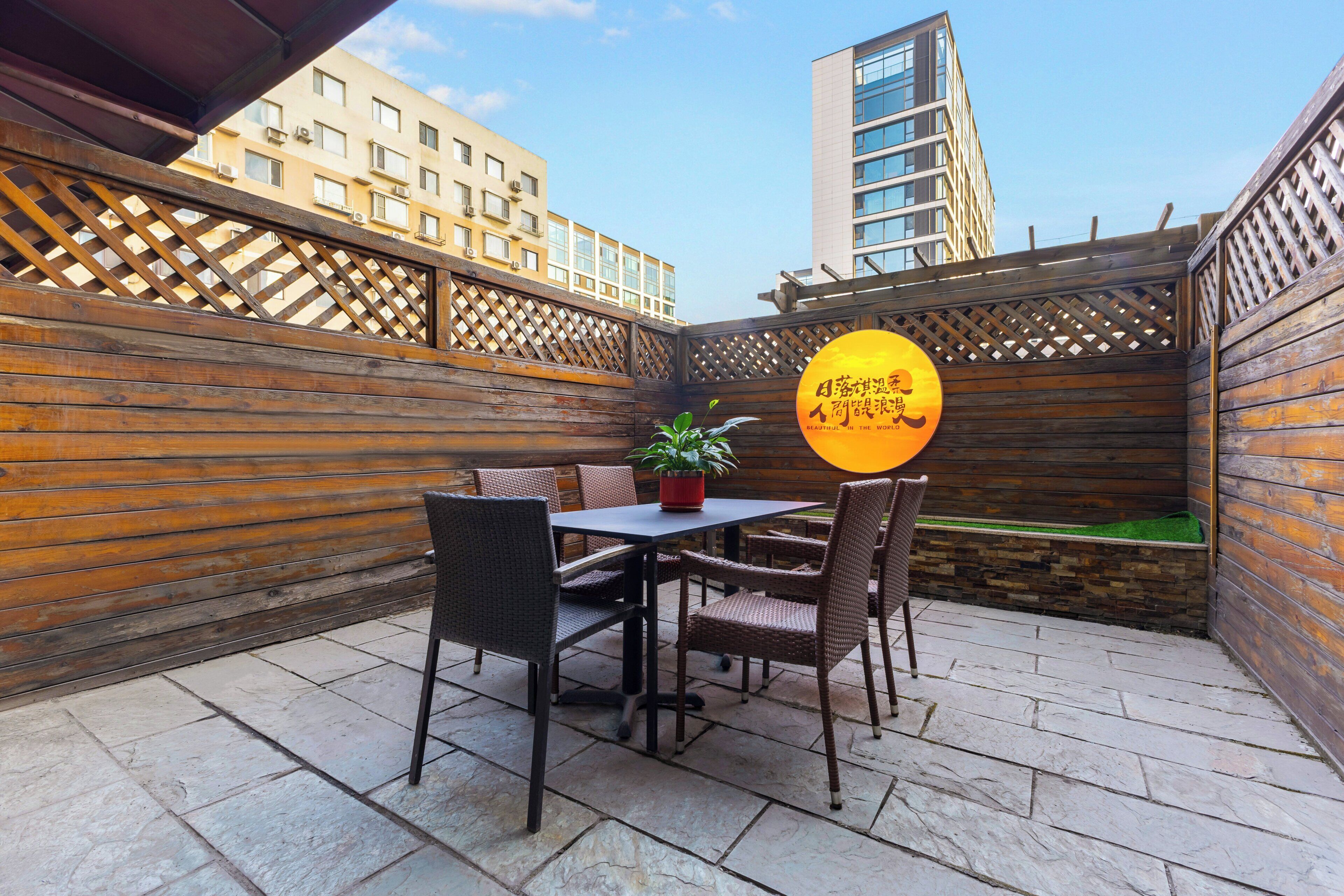 An outdoor patio with a table and chairs, a potted plant, and a wooden fence.