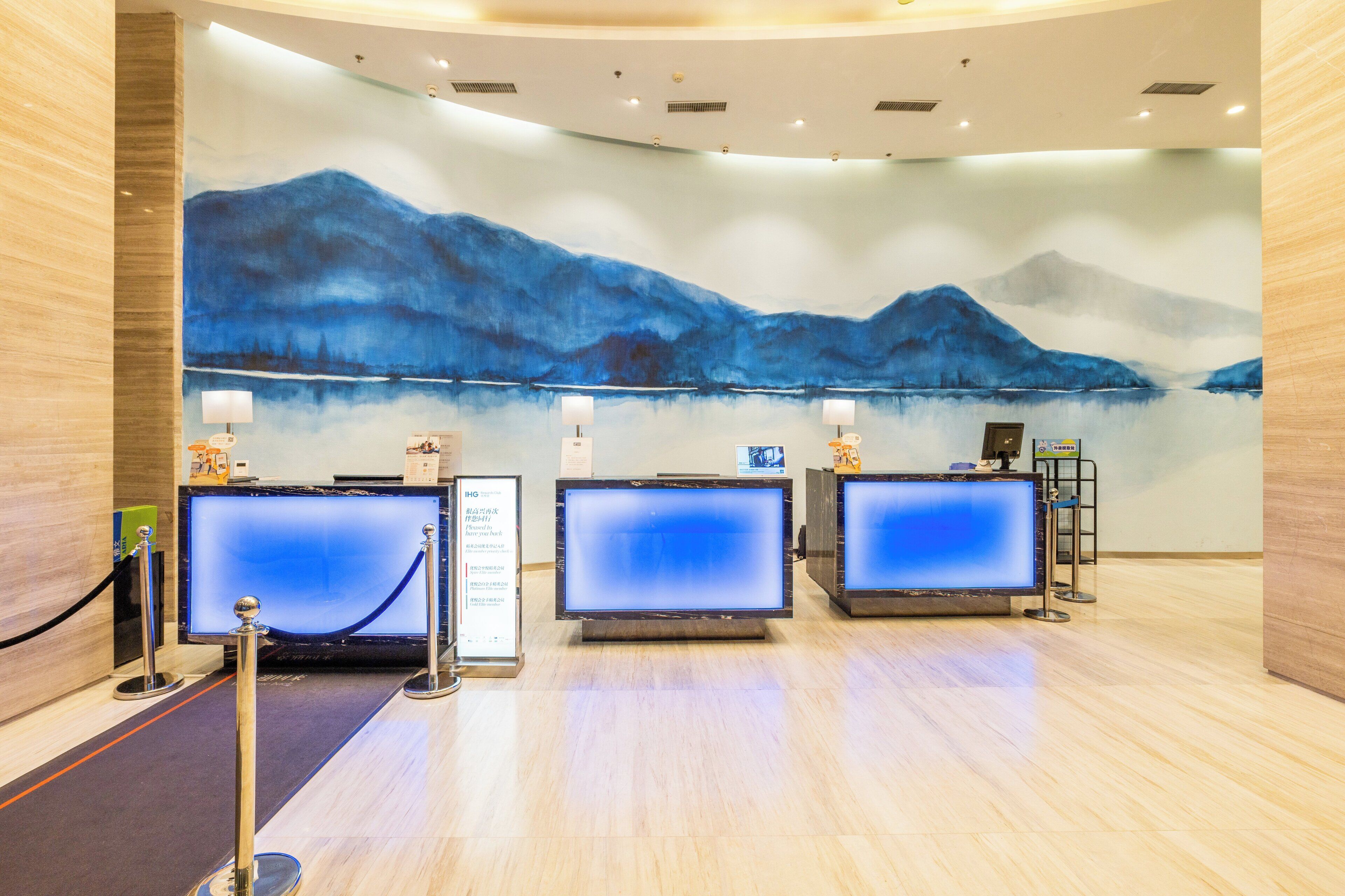 A reception area with three computer monitors, a large wall painting of mountains, and a wooden floor.