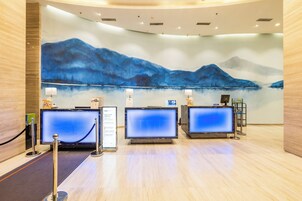 A reception area with three computer monitors, a large wall painting of mountains, and a wooden floor.