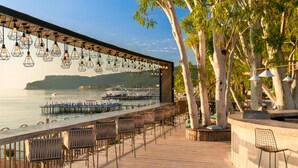 Un bar frente al agua con terraza, vista al mar e iluminación colgante.