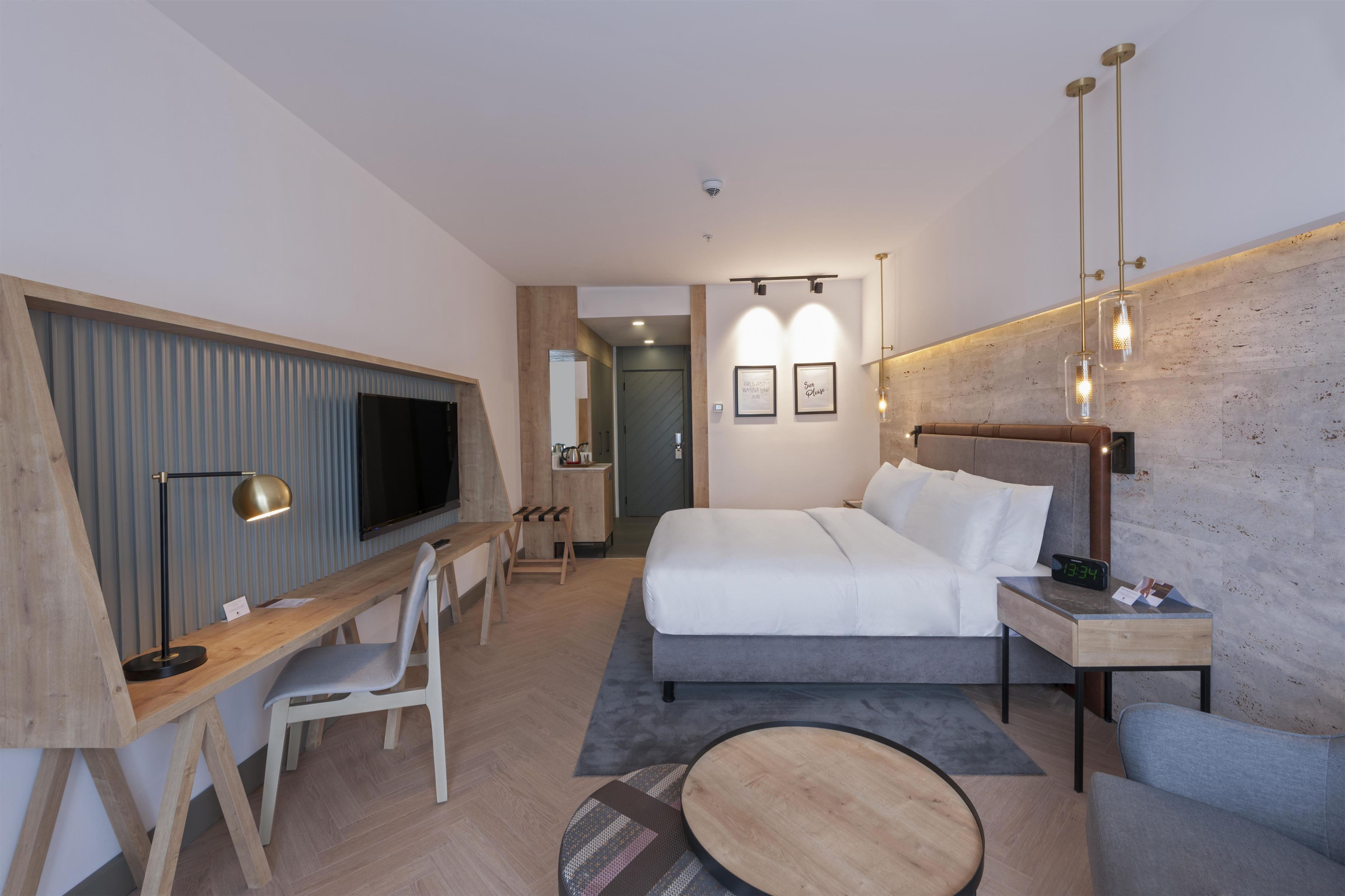 A modern hotel room with a bed, desk, chair, and a television.
