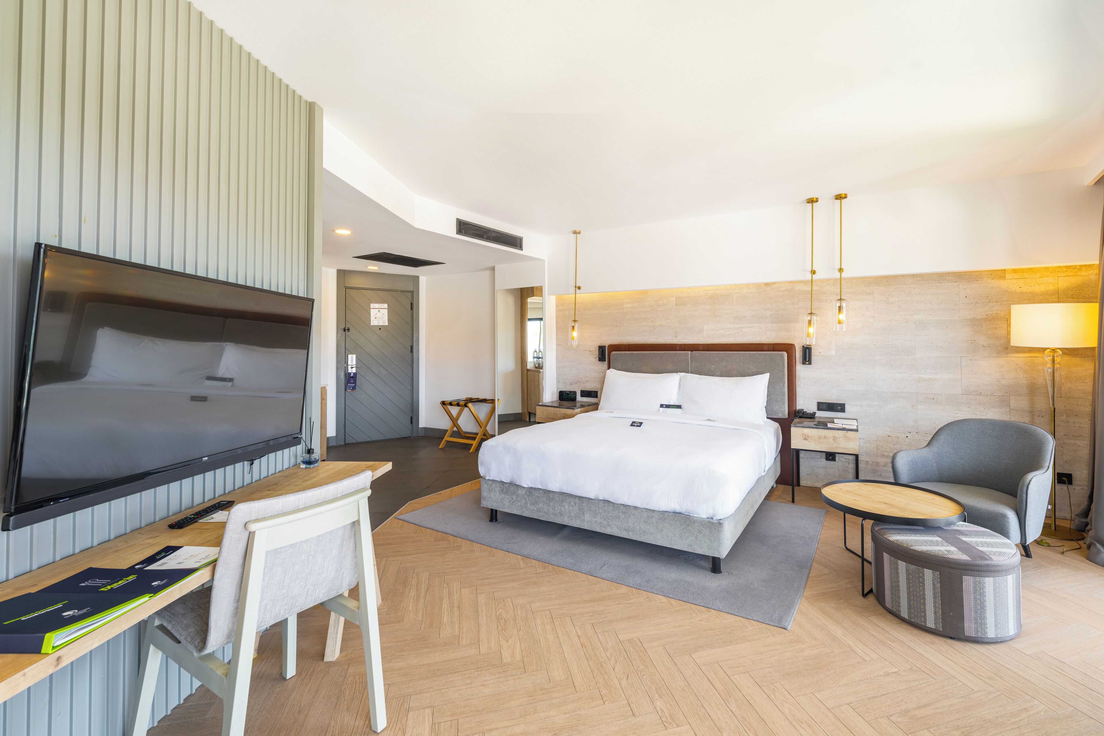 A modern hotel room with a large bed, a desk, a TV, and a chair.