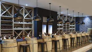 Una zona de bar con barriles de madera, taburetes y botellas de vino en estantes.