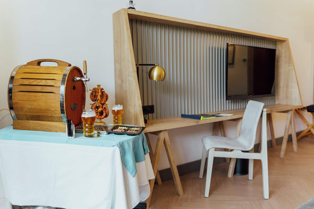 A room with a wooden desk, a chair, a television, a wooden barrel tap, and a table with a beer mug and snacks.