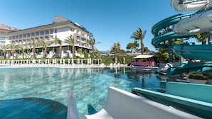 A resort pool with a water slide, palm trees, and a building with balconies.