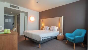 A modern hotel room with a large bed, a desk, a chair, and a bedside table.