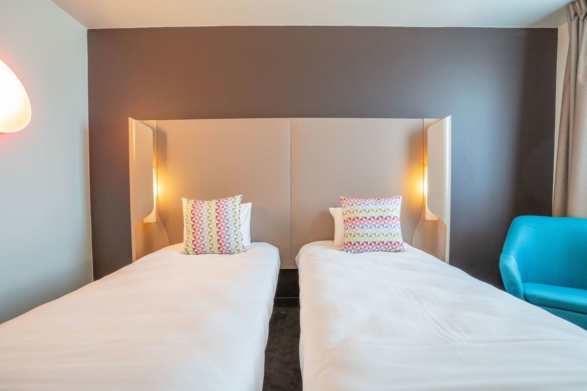 Une chambre d’hôtel avec deux lits simples, chacun agrémenté d’oreillers à motifs et de lampes de chevet.