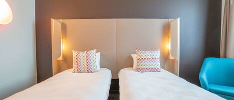 Une chambre d’hôtel avec deux lits simples, chacun agrémenté d’oreillers à motifs et de lampes de chevet.