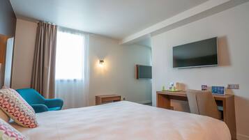 Une chambre d’hôtel avec un grand lit, un bureau doté d’un téléviseur à écran plat, une chaise et une petite table.