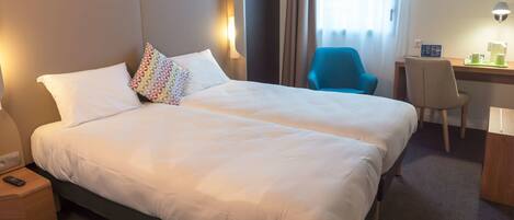 A hotel room with a large bed, a desk, a chair, and a nightstand.