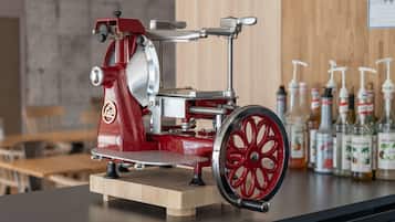 A vintage meat slicer on a wooden base with a counter behind it displaying various bottles.
