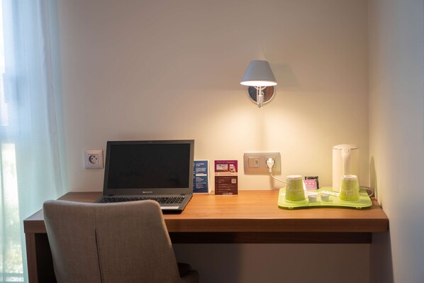 A hotel room with a wooden desk, a laptop, a lamp, and a green tray with items on it.