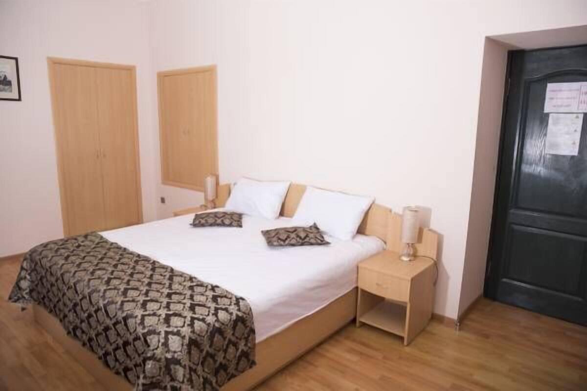 Une chambre à coucher avec un lit, deux tables de chevet, une porte en bois et un tableau encadré au mur.