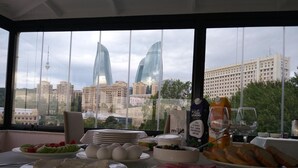 Una mesa de desayuno con diversos alimentos y una botella de leche, frente a una vista de la ciudad con edificios modernos.