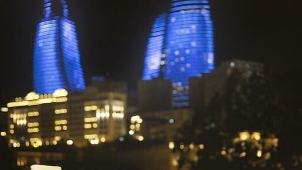Un comedor con una mesa y sillas, vista de edificios iluminados por la noche y una ventana con vistas a la ciudad.